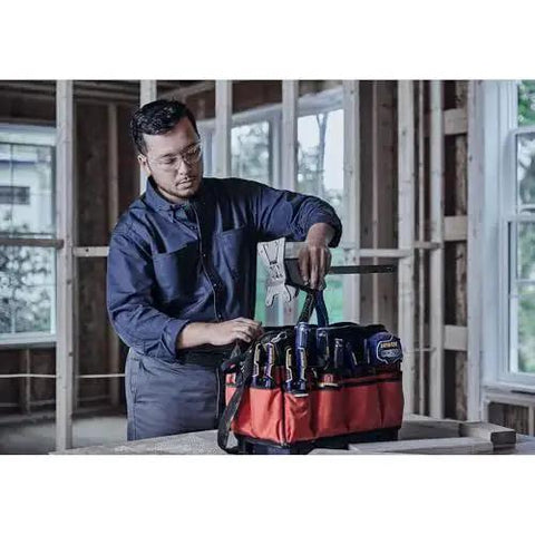Person organizing tools in a red and black tool bag at a construction site with wooden framing.