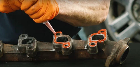 Permatex 81630 Ultra Red gasket maker being applied to gasket surfaces on an automotive metal intake component