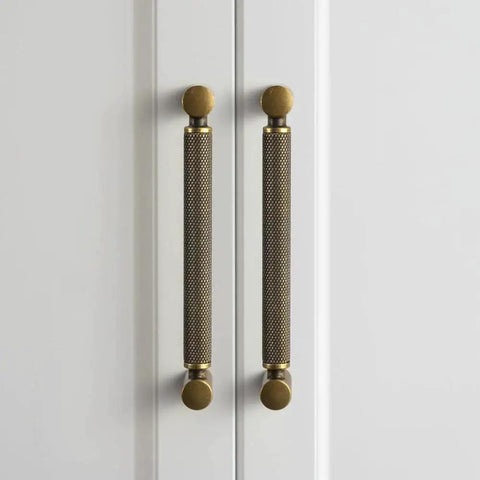Front view of Six Pack 5 Inch Center To Center Antique Brass Cabinet Pulls With Knurled Grip And Circular End Caps on white doors.