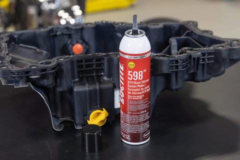 598 Black High Temp RTV Silicone Sealant For Auto Use OEM Approved Performance Engine Building And Repair Grade Heat Resistant Adhesive Sealant Durable Gasket Maker For Intake Exhaust And Engine Surfaces shown beside an engine part.