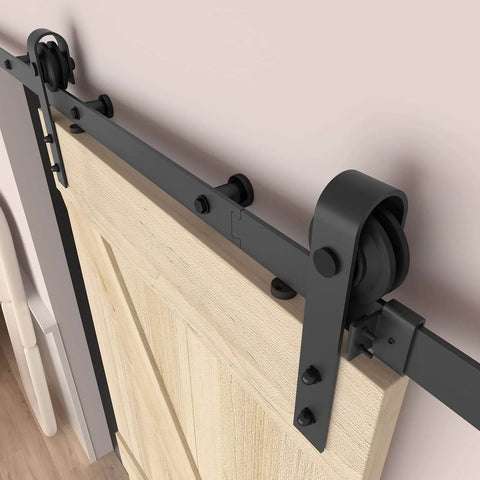 5FT Barn Door Hardware Kit with Heavy Duty Modular Sliding Track installed on light wood door, J Shaped Carbon Steel System in room.