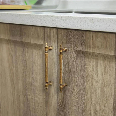 Six Pack 5 Inch Antique Brass Cabinet Pulls With Ornate Tapered Handles Decorative Finials And Sculpted Detailing shown installed on wooden cabinets.