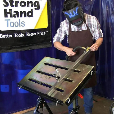 Person welding on worksite ready welding table pro grade with 1.1 inch slot top adjustable height and tilt casters.