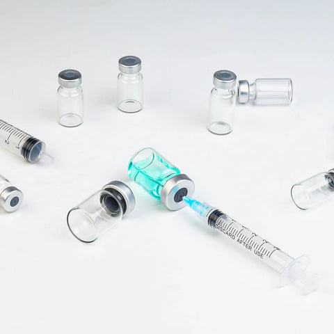 Several 5ml glass injection vials with metal caps; transparent, sealed, empty vials around a syringe with blue liquid.