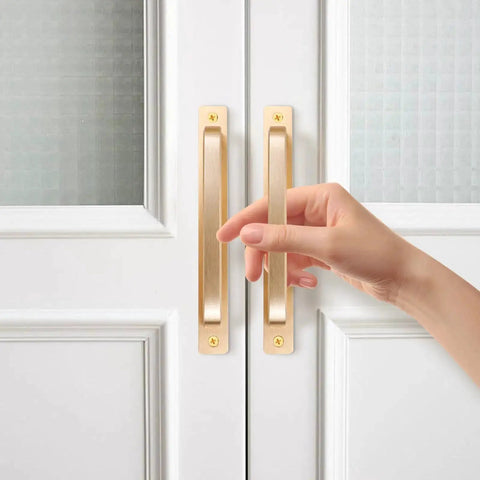 Close-up of hand on 2 Pack Barn Door Handles for Cabinets and Drawers, Aluminum Alloy Flush Flat Base Pulls in Gold, installed on white door.