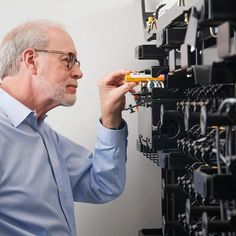 Fiber optic cable tester (orange handheld) being used beside a server rack with bundled fiber cables.