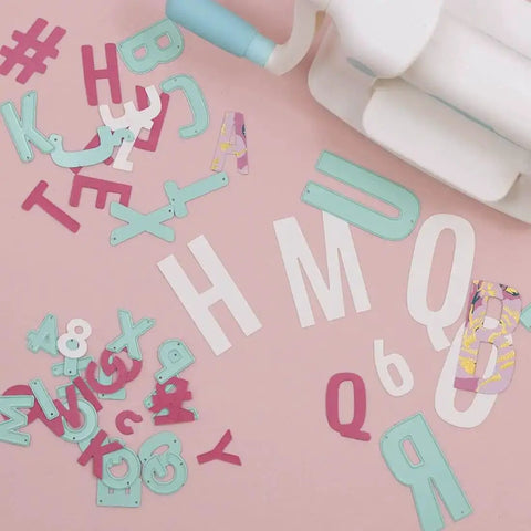 Number Shaped Die Cut Set, 0 Through 9, scattered letters and numbers next to a die cutting machine on a pink background