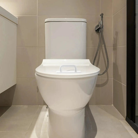 Front view of a toilet in a modern bathroom setting with beige tiles and a handheld bidet sprayer visible on the side.