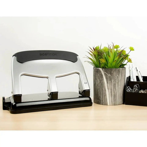 EZ Squeeze Heavy Duty 3 Hole Punch With 40 Sheet Capacity, All Metal Build next to potted plant and office supplies on desk