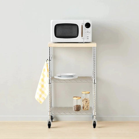 Metal wire kitchen cart with microwave, plates, and jars, on wheels, against a white wall.