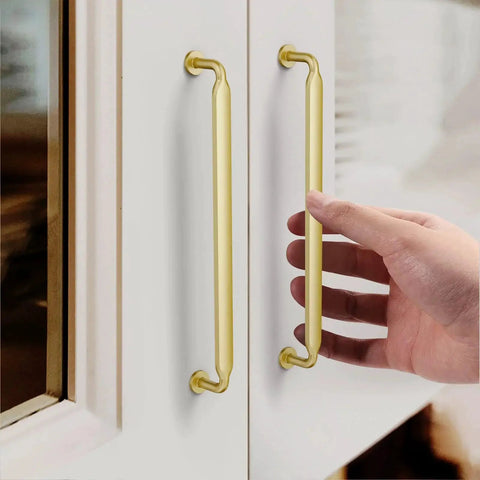 Hand touching Gold Cabinet Pulls 7.5 Inch 10 Pack Zinc Alloy Handles for kitchen cabinets with satin gold finish installed on white cabinet doors.