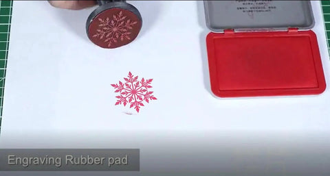 Rubber stamp pad with engraved snowflake design next to red ink pad on table.