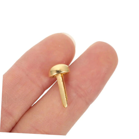 Close-up of a single golden paper fastener for scrapbooking projects, shown between fingers for scale.