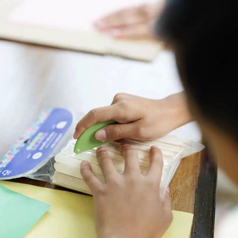 Person using Ceramic Micro Safety Cutter Keychain Box Opener 2 Pack Green to open plastic packaging on a table.