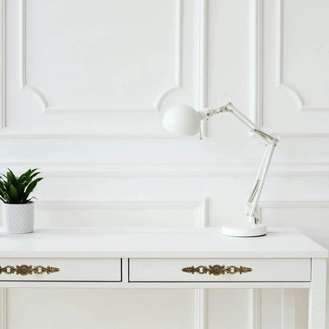 White desk with Vintage Bronze Patina Finish Cabinet Hardware Set floral pulls, lamp, and plant, in bright room with paneled wall.