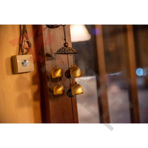 Interior view featuring golden wind chimes hanging near a wooden wall beside a square light switch with a metallic button.