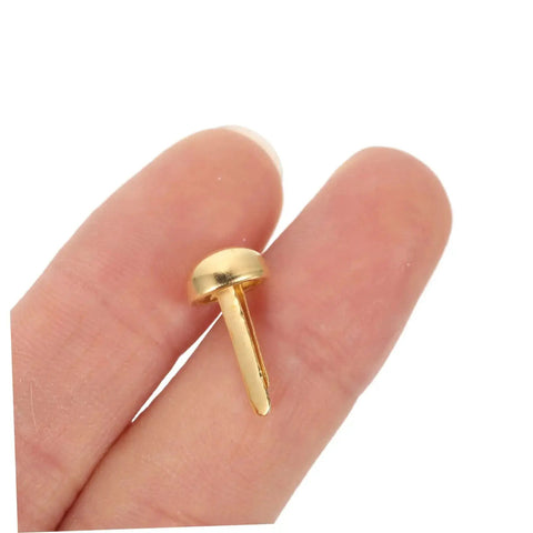 Close-up of a single brass paper brad held between fingers, part of the Must Have 100 Piece Paper Fasteners Brads For Scrapbooking And Card Making set.