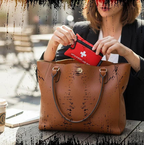 Woman placing Compact 20 Piece First Aid Kit with Carabiner into a brown leather handbag for travel and outdoor emergencies.