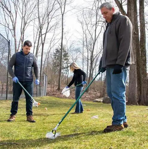 People using the 36 Inch Nifty Nabber Reacher Grabber Tool for easy yard cleanup and trash pickup in a grassy outdoor area.