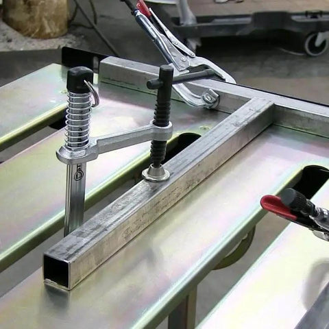 Close-up of Worksite Ready Welding Table Pro Grade With 1.1 Inch Slot Top Adjustable Height And Tilt Casters For Easy Mobility Retractable Guide Rails Eccentric Leveling Feet Three Position Angled Tabletop For Horizontal 30 Degree Or Folded Storage Use showing clamped setup.