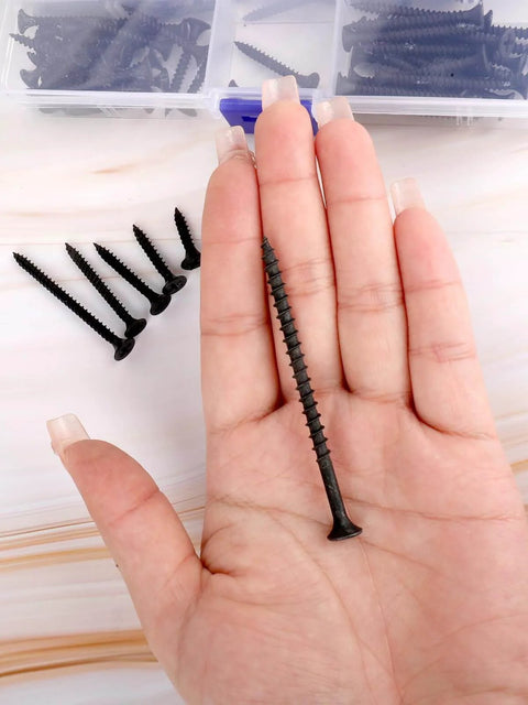 Close-up of hand holding black screw from Drywall Screws Assortment Kit, 166-Piece Black Wood Screws For Drywall, 6 Sizes