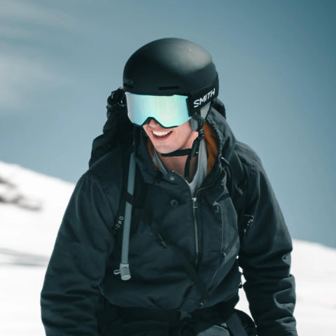 Outdoor climber wearing a black helmet and SMITH mirrored goggles in a snowy alpine landscape