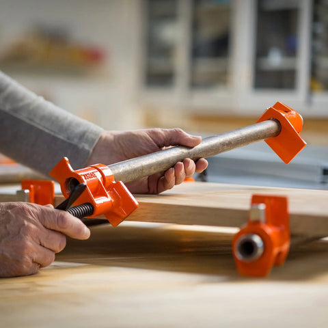 PONY two-pack orange wood gluing pipe clamp fixtures gripping a 3/4 inch pipe on a wood workbench