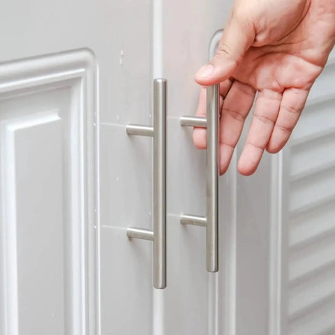 Hand approaching stainless steel T bar cabinet handles with satin brushed nickel finish, installed on white cupboard doors.