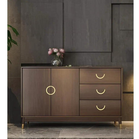 Stylish cabinet with golden copper hardware handles, wooden finish, three drawers, and decorative flowers on top.