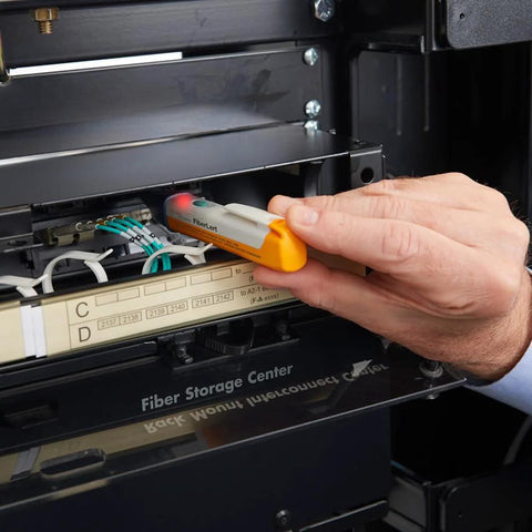 FiberLert-125 fiber optic tester and detector, orange and gray handheld device used in a fiber storage cabinet.