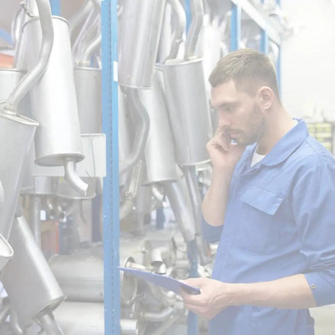 Mechanic in blue overalls examining car exhaust parts in warehouse
