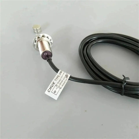 Front view of M12 normally open proximity sensor with cable, metal threaded body; magnet shown nearby