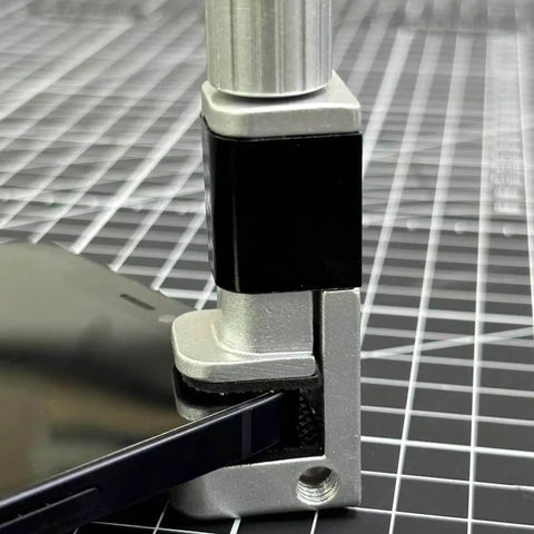 Close-up of adjustable screen repair clamps kit for phones and tablets holding a device screen securely on a grid surface.