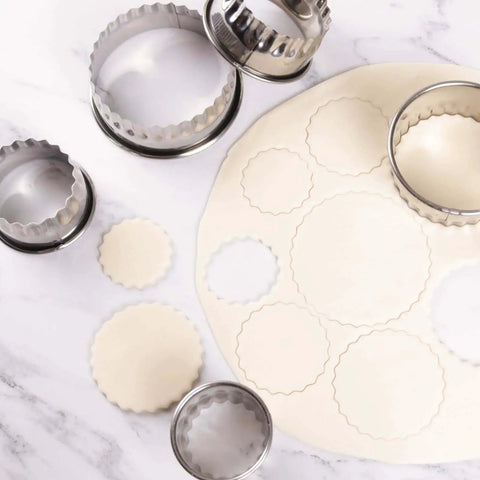 Fluted Round Cookie Cutter Set With Scalloped Biscuit And Circle Crinkle Cutters In Five Sizes Two Inch Through Three And A Half Inch Heavy Duty Food Grade Stainless Steel Rust Resistant With Comfortable Rolled Rim For Easy Handling in use on dough.