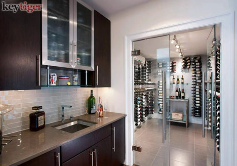 Modern kitchen with dark wood cabinets, stainless steel sink, and glass door leading to a wine room with racks filled with bottles.