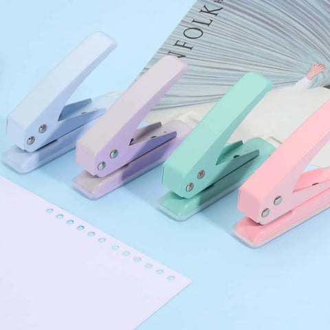 Set of colorful handheld paper punchers on blue background next to punched paper and magazines for DIY crafts and tags.