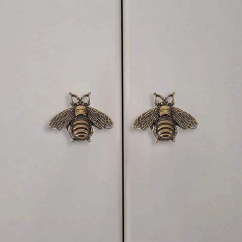 Close-up of two vintage gold bee shaped cabinet knobs on white cabinet doors, part of a set of 10 vintage gold bee shaped cabinet knobs made from zinc alloy hardware for cabinets and dressers retro bronze finish drawer knobs pull handles for dresser drawers durable rust resistant and stylish cabinet hardware.