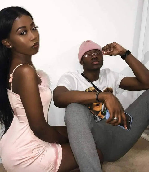 Two individuals sitting indoors, one wearing a pink dress, the other in grey pants and a pink beanie, showcasing casual style.