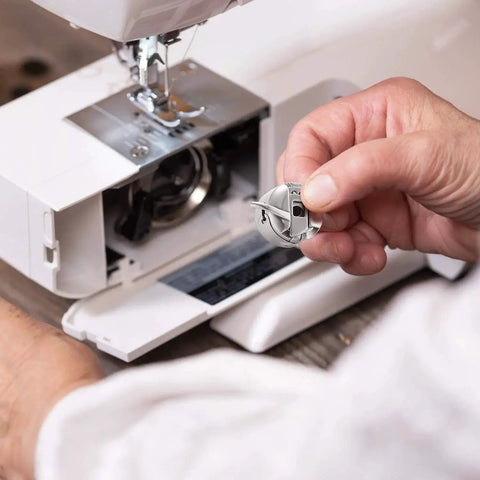 Close-up of a stainless steel sewing machine bobbin case for front-loading machines, held in hand.