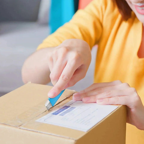 Person using Retractable Box Cutter Utility Knife 12 Pack All Metal Shell Single Edge Blades to open a cardboard box.