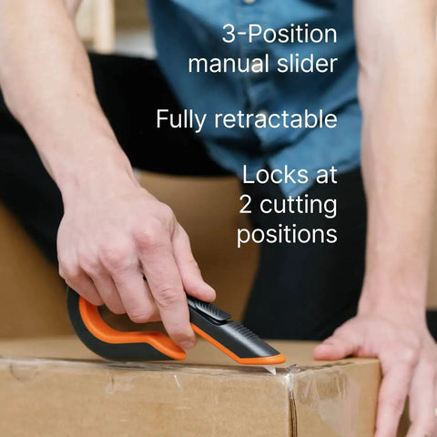 Person using 3 Position Box Cutter With Ceramic Zirconia Blade And Locking Blade on cardboard box. Visible manual slider in orange and black.