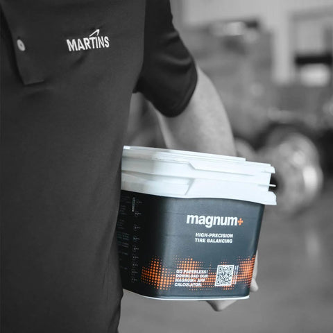 Person holding container of tempered glass tire balancing beads, labeled Magnum+, for pro install; no wheel weights needed.
