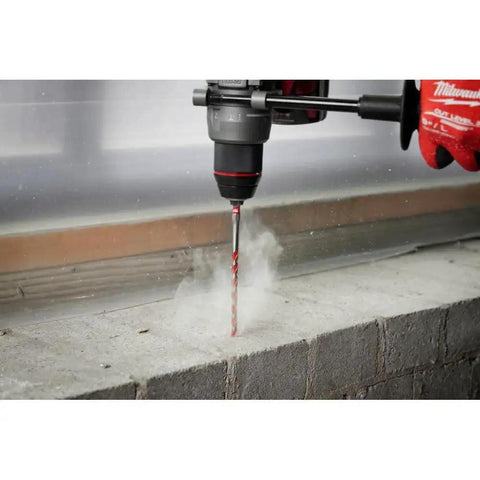 Shockwave Impact Duty 10 Piece Carbide Hammer Drill Bit Set For Concrete Block And Brick With One Quarter Inch Hex Shank 4X Faster Drilling Dynamic Cutting Edges Longer Life Milwaukee in action drilling a concrete block with visible dust.