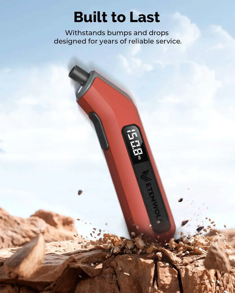 Digital Tire Pressure Gauge T300 3-200 PSI Calibrated to ANSI B40.7 Grade 2A With Replaceable AAA Batteries In Vivid Orange side view on rough terrain.