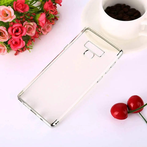 Clear smartphone case with open cutouts on a white surface surrounded by flowers, coffee cup, and cherries