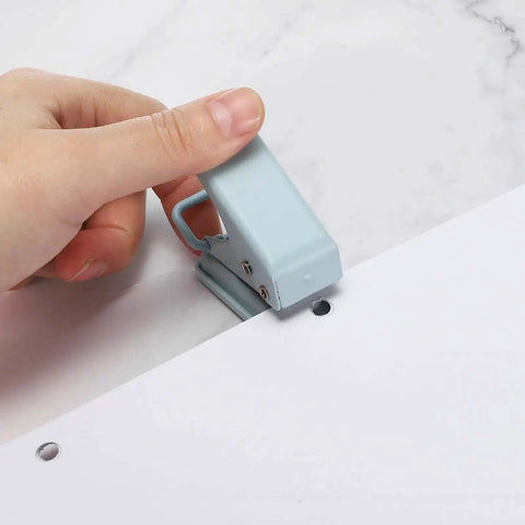 Person using a handheld hole punch on paper, creating a 6mm hole. Heavy Duty Handheld Hole Punch One Quarter Inch For Paper Craft Scrapbook Tags And Tickets.