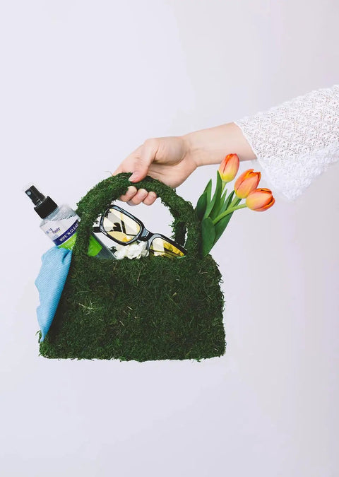 Streak Free Eyewear Screen And Lens Cleaner Spray For Glasses And Cameras in a grass bag with sunglasses and flowers.