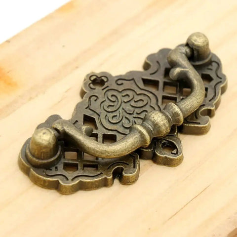 Image of a vintage antique brass bail pull handle mounted on wood, features a decorative hollowed pattern, part of 4 pack, 2.6x1.5 inches, zinc alloy.