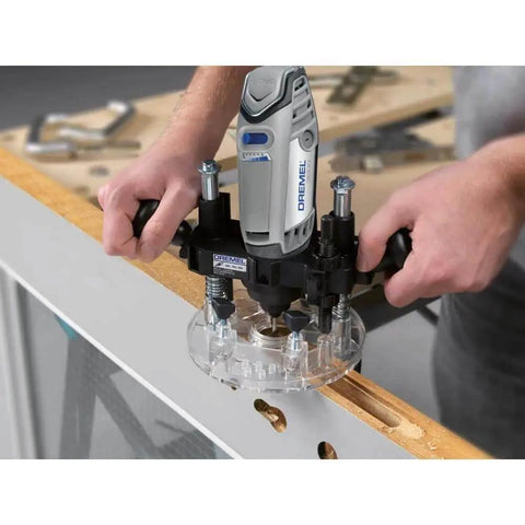 Person using Compact Plunge Router Attachment For Dremel Rotary Tool Lets You Cut Decorative Edges, Straight Slots And Circles And Inlay Work With Depth Adjustable Up To 1.875 Inches For Small To Medium Woodworking Projects on wooden surface in workshop.