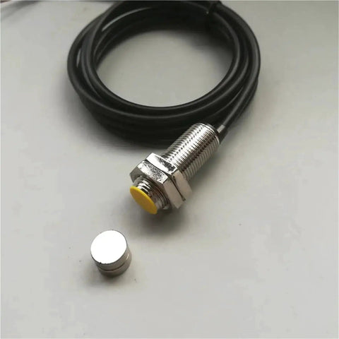 Front view of M18 proximity sensor with yellow actuator, threaded metal body, and attached cable; separate magnet shown.